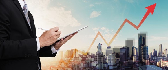 Businessman working on a digital tablet, with a city panorama and a raising arrow as a backdrop.