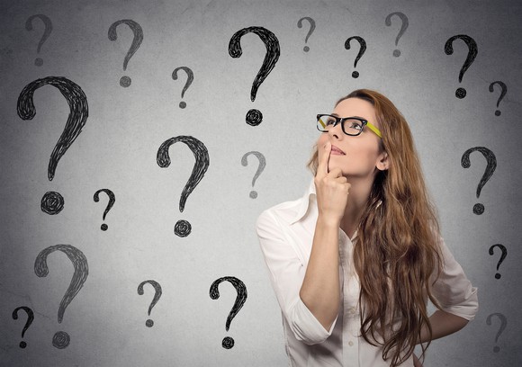 Business woman with glasses looking up at many question marks.