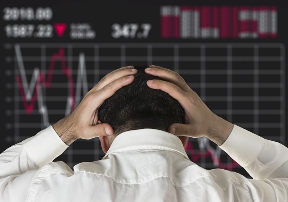 A man looking at a declining stock price chart holds his head in his hands.