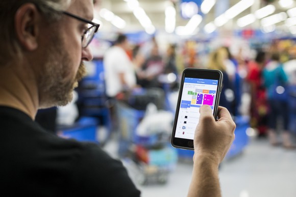 A man holds his phone with the Wal-Mart app open in a Wal-Mart