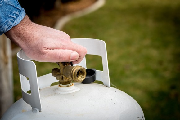 A person screwing the top of a propane tank.