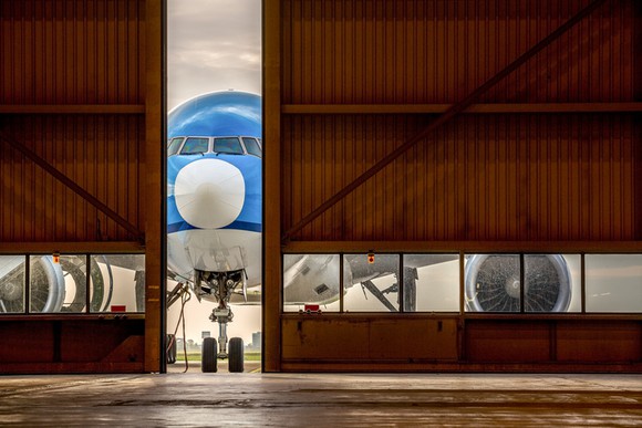 Blue plane in front of half-open hangar door, waiting to enter.