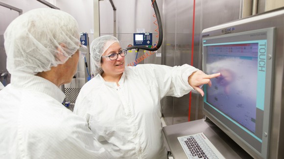 Prescription drug manufacturing employees at Johnson & Johnson pointing to a digital screen.