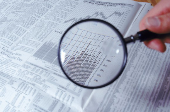 A magnifying glass being held over a financial newspaper.