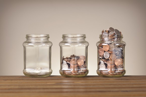 Three jars are lined up on a table, filled with increasingly larger amounts of coins.