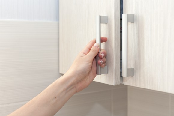 A hand pulls a cupboard door open.
