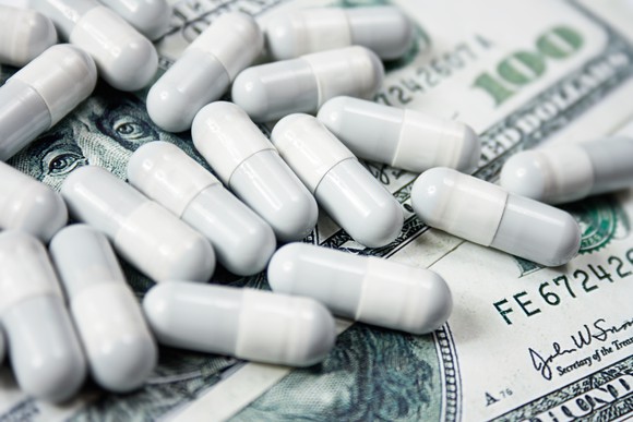 Prescription drug capsules atop a pile of cash.