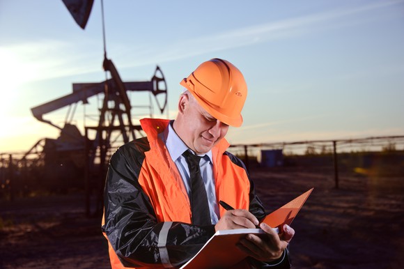 A man writing in a notebook standing in front of an oil well.