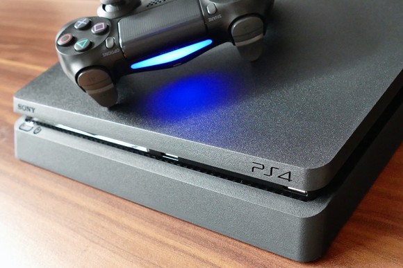 Sony Playstation 4 console laying on top of wooden table with controller laying on top of the console and powered on.