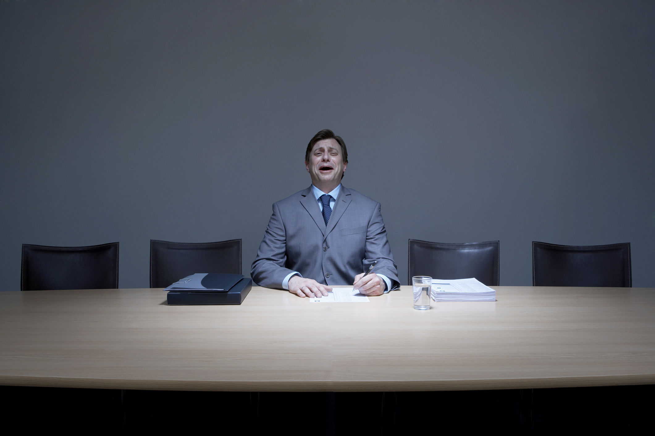 Businessman working alone in boardroom, crying, portrait