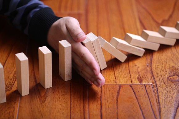 A hand stops a row of dominoes from falling.