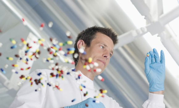 Lots of pills with scientist holding one pill