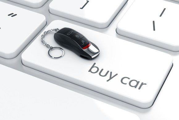 A key fob sits atop a "buy car" button on a computer keyboard.