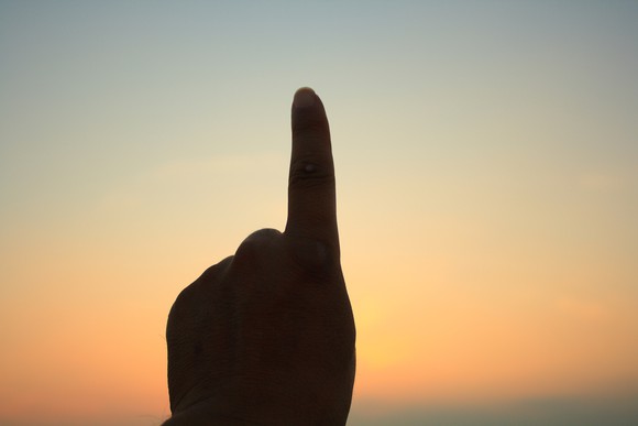 A finger points upward, silhouetted against the sunset.