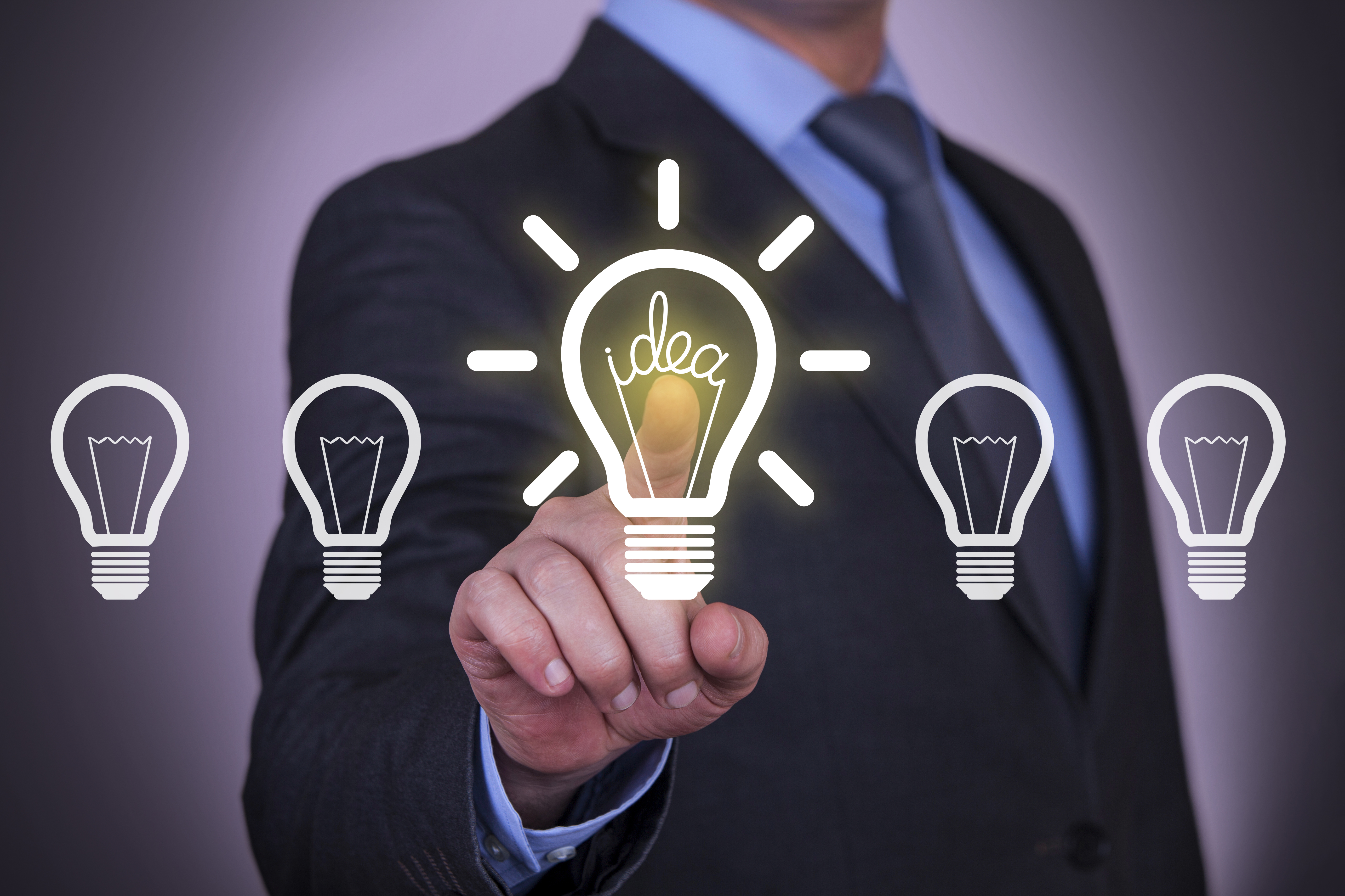 A business person points at a lit up light bulb among a row of unlit light bulbs.