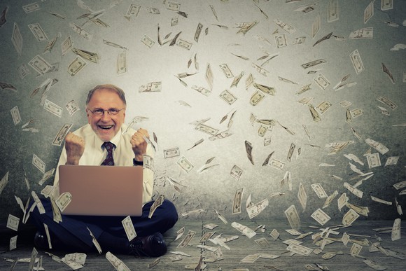 Senior man with a laptop and money falling from the sky