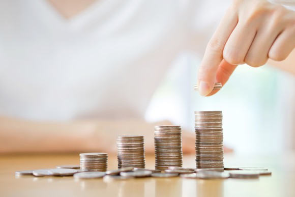 A person prepares to place a coin on the tallest of successively higher stacks.