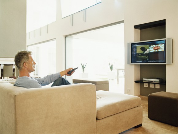 Man sitting on couch flipping channels on TV.