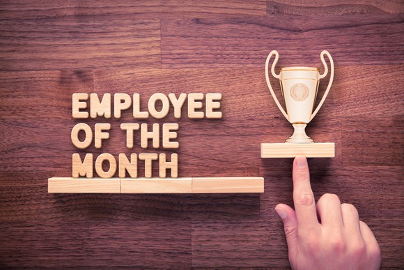 A finger points to a wooden trophy, which sits next to the words "Employee of the Month."