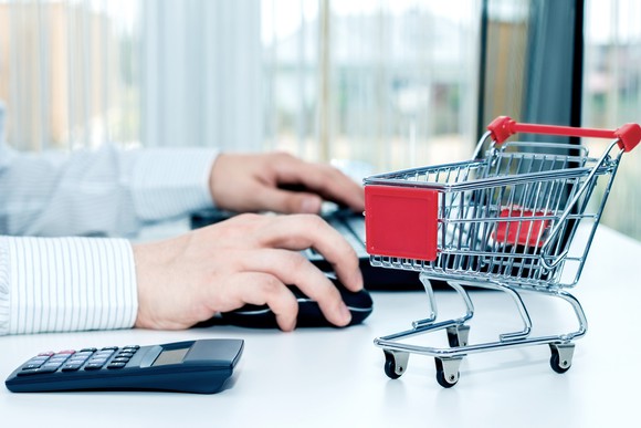 Man working at computer with calculator and a model of a shopping cart next to him.