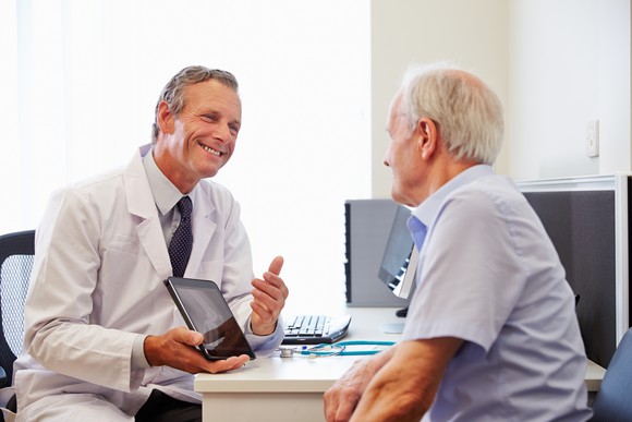 A doctor consulting with a patient and using a tablet. 