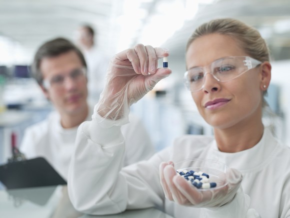 A pharmaceutical lab researcher holding and examining a capsule.