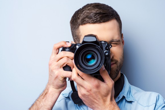 Man facing viewer with camera, about to take photo.