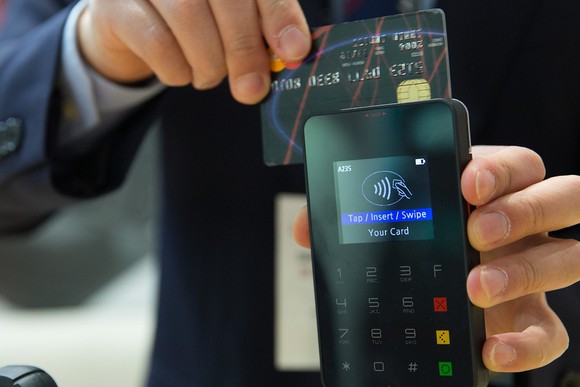 Man in suit swiping credit card through payment terminal.