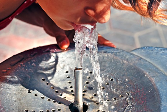 Young person drinking from a water fountain.