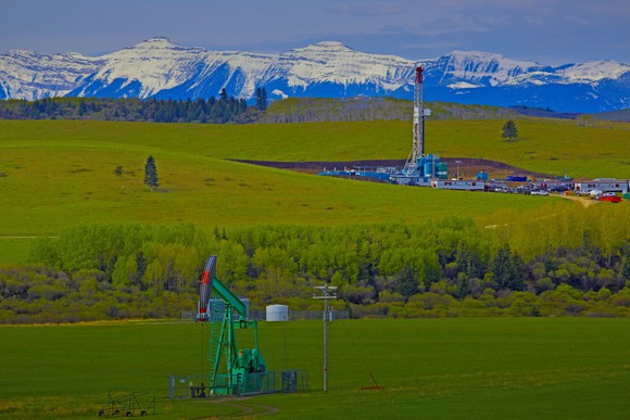 Drilling rig and pump jack with mountain range in background