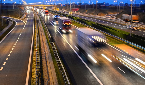 Long exposure shot of commercial trucks on highway at dusk.