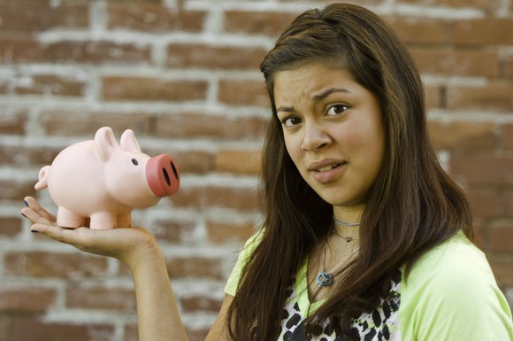 A confused young adult holding a piggy bank.