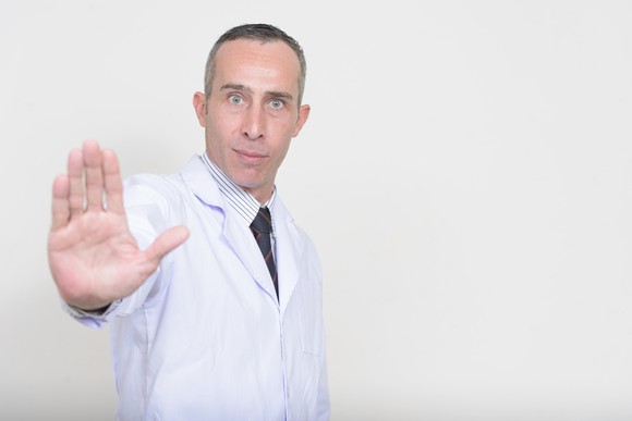 A doctor with an outstretched arm, as if signaling someone to stop.