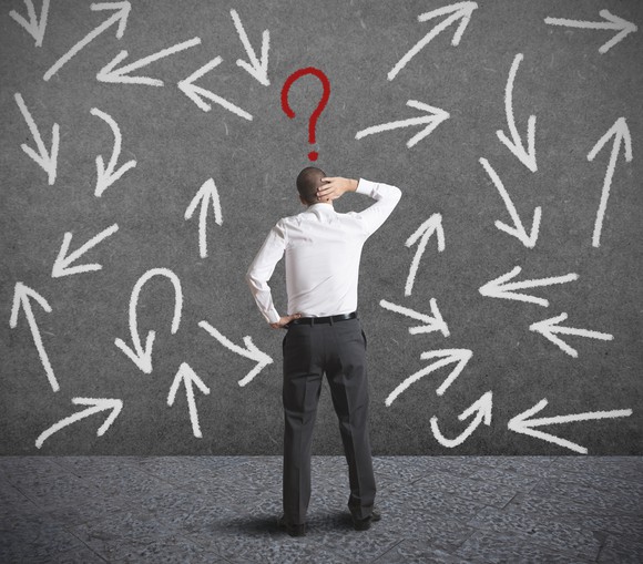 A man, seen from behind, stands facing an assortment of arrows pointing in various directions, as a red question mark floats above his head.