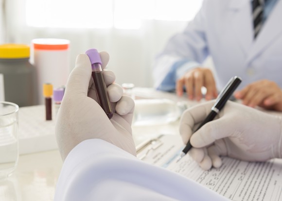 A biotech lab researcher examining a blood sample and taking notes.