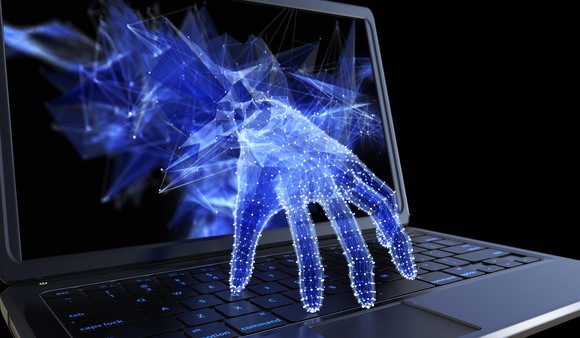 A hand reaching out from a computer screen to touch the keyboard.
