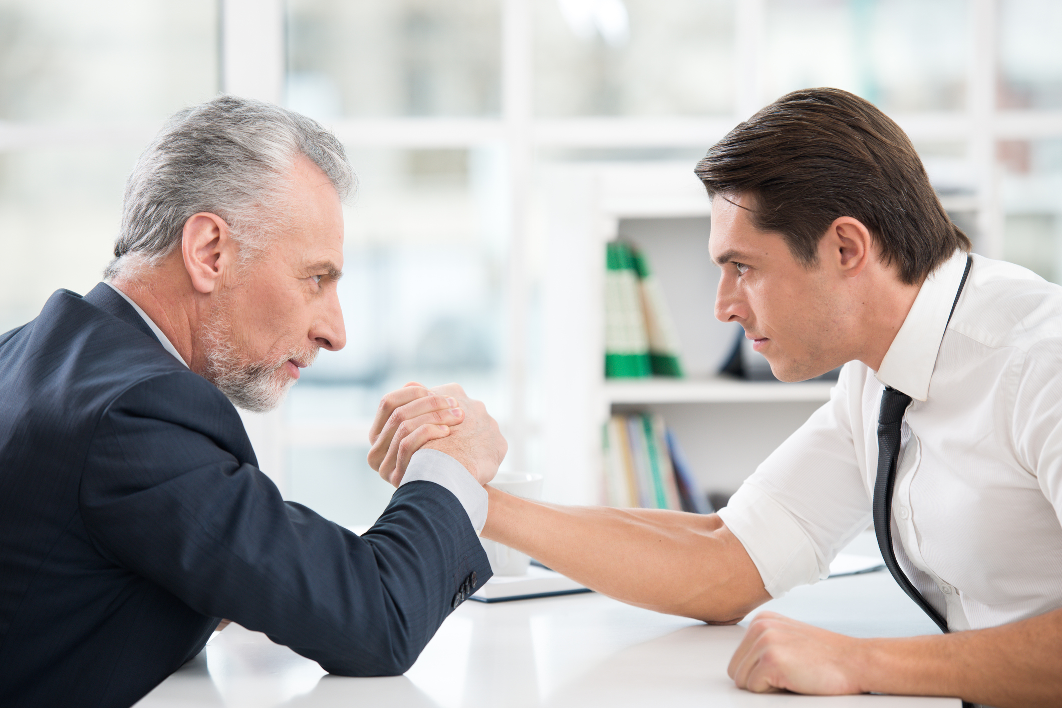 Two businessmen arm wrestle.