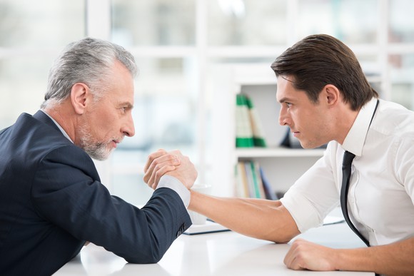 Two businessmen arm wrestle.