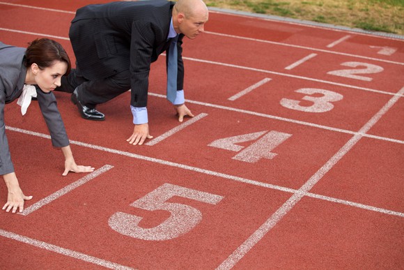 A businessman and woman crouch in starting position at the start of a running track.