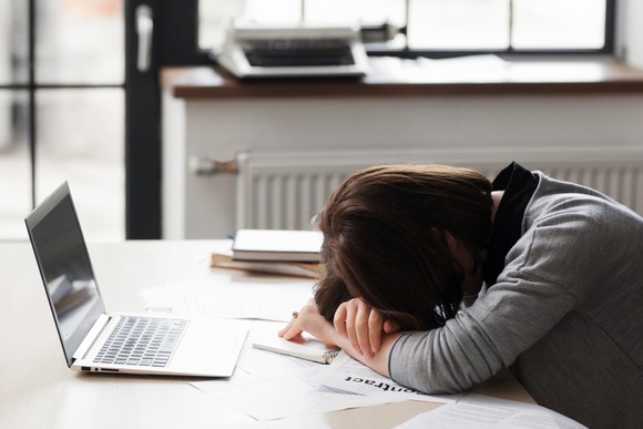A woman puts her head down on her desk.