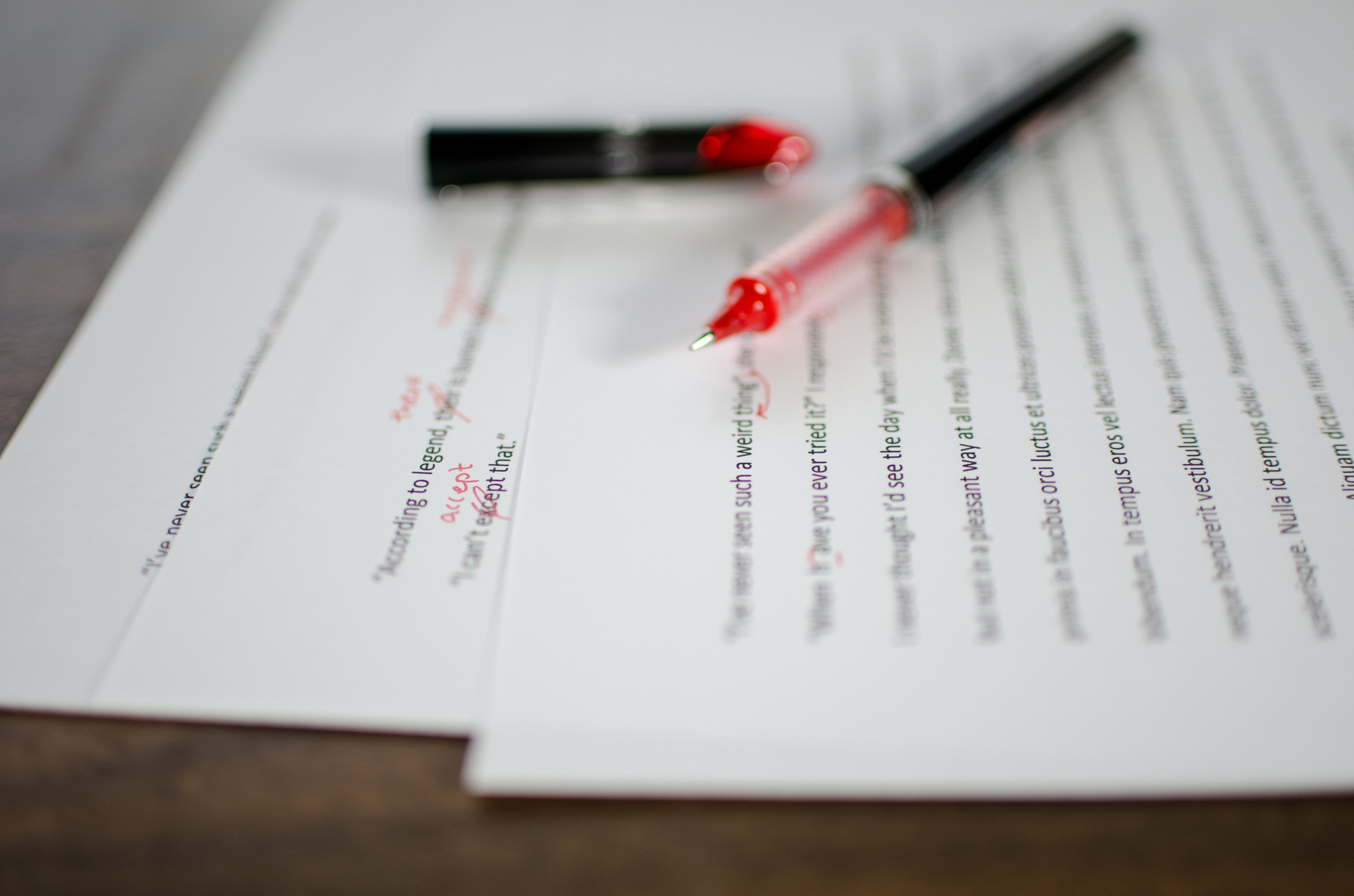 A red pen sits on papers with red edit marks.