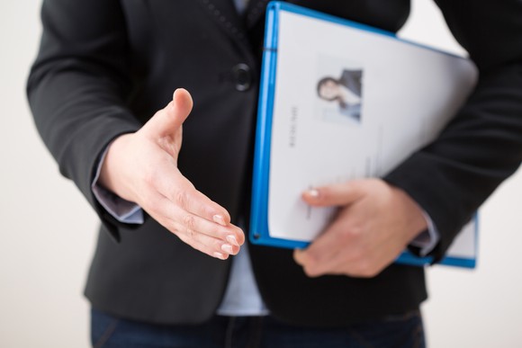 A person holding a folder puts a hand out to shake.