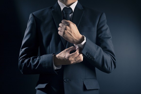 A man in a sut fixes his cuff.