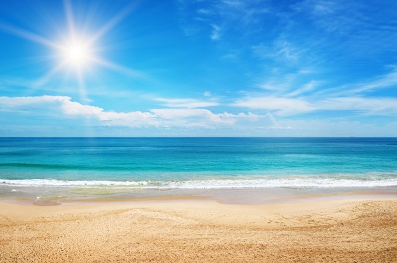 A beach with the sun shining in the background.