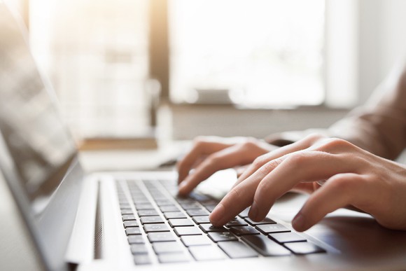A side view of hands typing on a laptop keyboard.