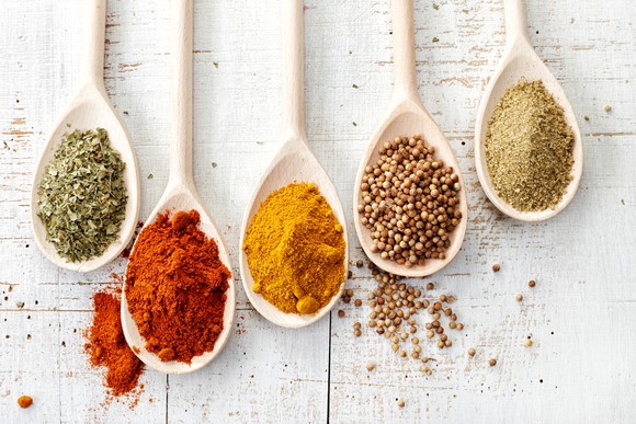 Five spoons are lined up side by side, each filled with a different spice.