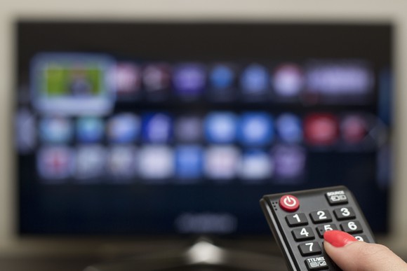 A woman's hand points a remote control at a TV.