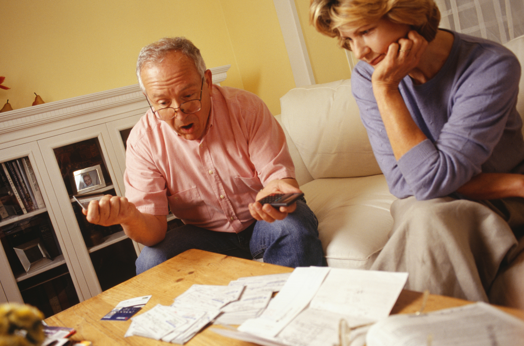 Couple sitting by table covered in papers, looking worried.