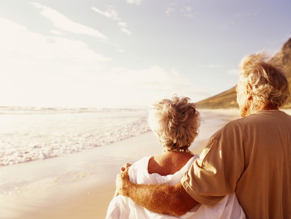 Elderly man with arm around elderly woman on a beach, facing the sunset