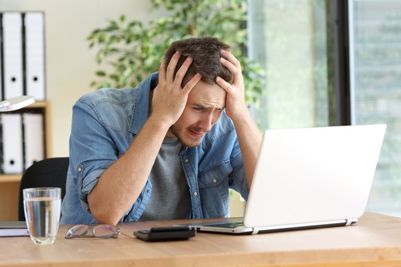 man at desk frustrated at laptop pulling his hair out